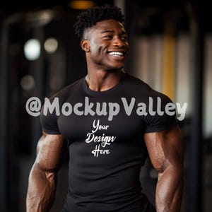 May include: A black t-shirt with the text "Your Design Here" on the front. The shirt is being worn by a person with a muscular build. The background is blurry and appears to be a gym.
