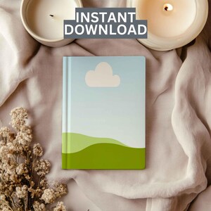 May include: A green and blue notebook with a white cloud and green hills design. The notebook is lying on a light brown fabric surface with two white candles.