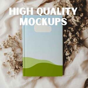 May include: A light blue book mockup with a white cloud and green hills on the cover. The book is lying on a white fabric background with dried flowers.