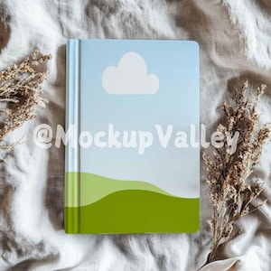 May include: A blue and green notebook with a white cloud and a green hill design. The notebook is lying on a white and brown fabric surface.