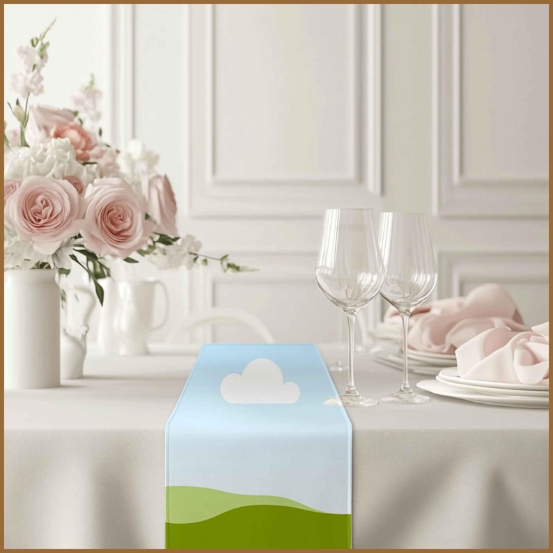 May include: A light blue table runner with a white cloud and green hills design. The runner is on a white tablecloth with two wine glasses and a pink napkin.