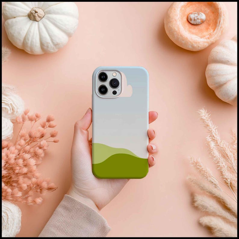 May include: A smartphone case with a landscape design. The case features a gradient of colors, starting with a light blue at the top, transitioning to white, and ending with green at the bottom. The case is held in a hand.