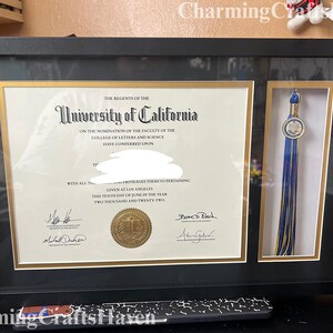 May include: A framed University of California diploma with a gold seal and a blue and gold tassel. The diploma is in a black frame with a gold border. The text on the diploma reads "University of California".