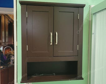 May include: A dark brown wooden wall-mounted cabinet with two doors and a lower shelf. The cabinet has silver handles and is mounted on a green wall. The cabinet is designed for storage.