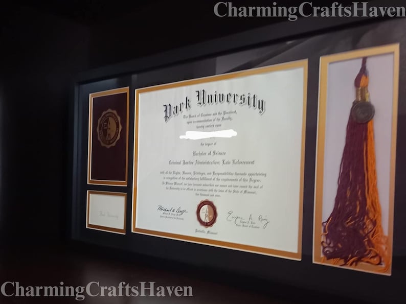 May include: A framed diploma from Park University, with a Bachelor of Science degree in Criminal Justice Administration. The frame also includes a tassel and a small document, all with gold accents.