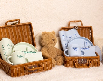 May include: Two wicker baskets filled with baby items. The basket on the left contains a green plate, two green cups, and a green bowl. The basket on the right contains a blue plate, two blue cups, and a blue bowl. The baskets are sitting on a white fluffy surface.