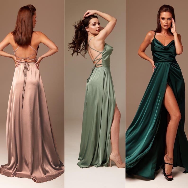 May include: Three women wearing long, flowing satin dresses in different colors: dusty rose, sage green, and emerald green. The dresses have a low back with a criss-cross strap detail and a high slit on the front.