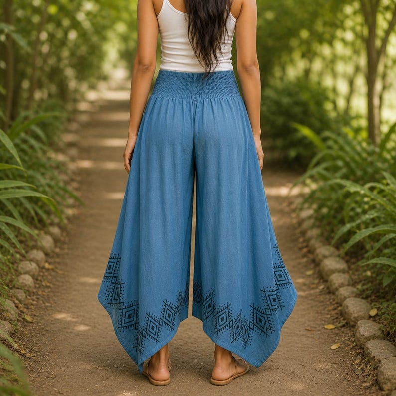 May include: Blue palazzo pants with a wide leg design and an elastic waistband. The pants feature a geometric pattern in black along the hemline. The model is wearing a white tank top and sandals.