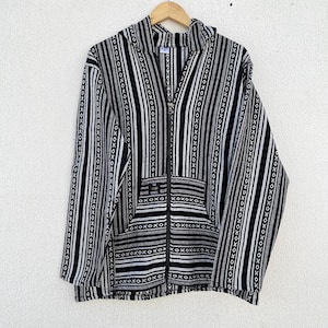 Könnte beinhalten: Ein schwarz-weiß gestreifter Kapuzenpullover mit Reißverschluss, Kapuze und Vordertaschen. Die Jacke hat ein vertikales Streifenmuster mit einfarbigen und gemusterten Streifen. Der Stoff scheint gewebt zu sein.