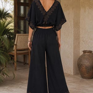 May include: Black two-piece outfit featuring a V-neck top with short sleeves and wide-leg pants. The top and pants have decorative patterns in a contrasting color. The outfit is made of a lightweight fabric, suitable for warm weather.