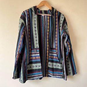 May include: A hooded jacket with a colorful striped pattern. The jacket features vertical stripes in black, blue, green, and red, with decorative diamond and zigzag patterns. It has two front pockets and a small patch with text.