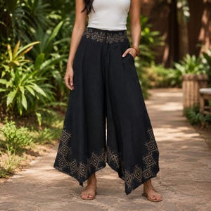 May include: Black palazzo pants with intricate gold geometric patterns at the waist and hem. The wide-leg pants have pockets and are paired with a white top. The pants are made of a flowing fabric, perfect for warm weather.