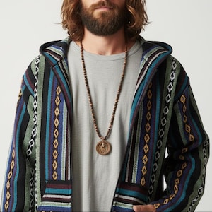 May include: A hooded jacket with a colorful striped pattern in shades of blue, green, black, and maroon. The jacket has a zipper closure and a wooden beaded necklace with a circular pendant. The person is wearing a gray t-shirt.