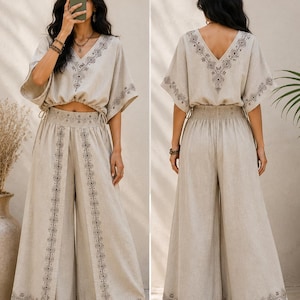 May include: A two-piece beige linen outfit featuring a V-neck top with short sleeves and wide-leg pants. The top and pants are adorned with intricate dark brown geometric embroidery. The outfit is designed with a relaxed fit, perfect for warm weather.