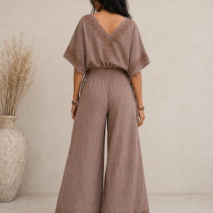 May include: A two-piece brown jumpsuit with a V-neck top and wide-leg pants. The top and pants feature embroidered details. The top has short sleeves and a drawstring waist. The pants have an elastic waistband and are floor-length.