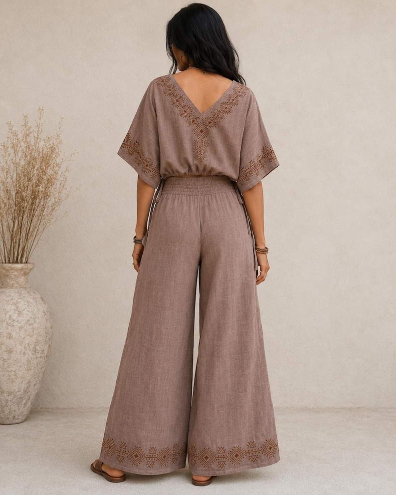 May include: A two-piece brown jumpsuit with a V-neck top and wide-leg pants. The top and pants feature embroidered details. The top has short sleeves and a drawstring waist. The pants have an elastic waistband and are floor-length.