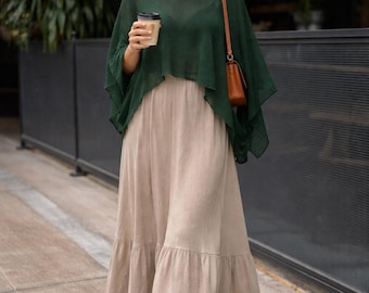 May include: A woman wearing a dark green top, a long beige skirt, and brown sandals. She is holding a coffee cup and wearing sunglasses. A brown purse hangs from her shoulder. The outfit is suitable for casual wear.