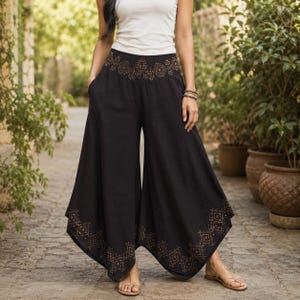 May include: Black palazzo pants with a wide leg and a decorative geometric pattern in a gold color at the waist and hem. The pants are paired with a white tank top and sandals.