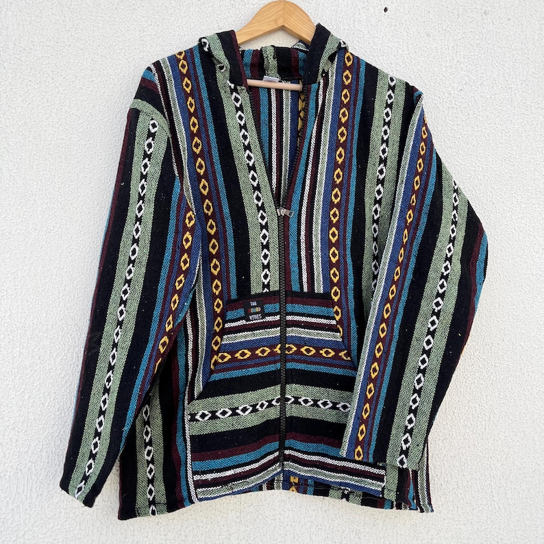 May include: A hooded jacket with a full zipper, featuring a striped pattern in black, blue, green, and red. The jacket has a front pocket and is hanging on a wooden hanger against a white background. The text "THE VIBES" is visible on the pocket.