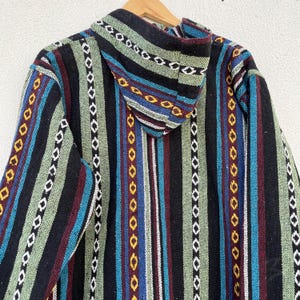 May include: A hooded jacket with a colorful striped pattern. The jacket features vertical stripes in black, green, blue, red, and white, with decorative stitching. The hood is also striped. The jacket is hanging on a wooden hanger.