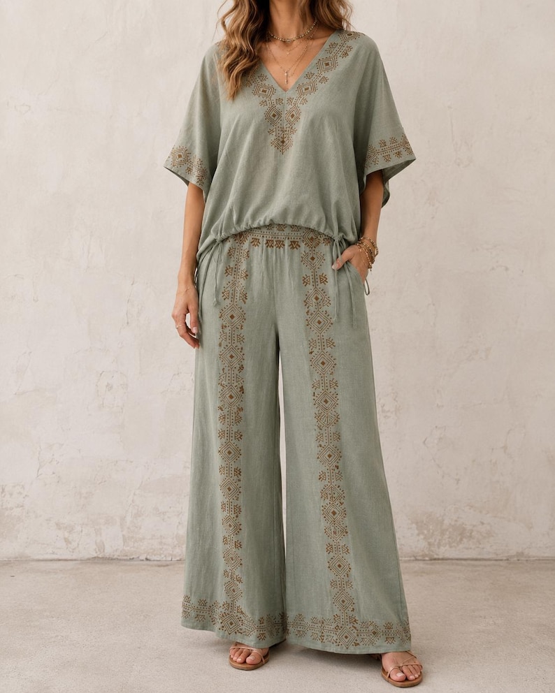 May include: Sage green two-piece outfit featuring a V-neck top and wide-leg pants. The top and pants have intricate embroidered detailing in a complementary color. The outfit is made of a lightweight fabric, perfect for warm weather.