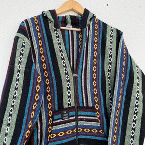 May include: A hooded zip-up jacket with a colorful striped pattern. The jacket features vertical stripes in black, green, blue, and maroon, with decorative diamond and oval patterns. The pocket has the text "THE GOOD VIBES".
