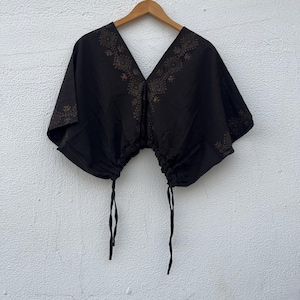 May include: A black short-sleeved top with a deep V-neckline and a drawstring hem featuring two hanging ties. The garment is decorated with a brown geometric pattern along the neckline and shoulders, creating a distinct contrast against the black fabric.