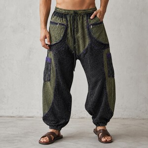 Op de afbeelding: Tweekleurige, olijfgroene en zwarte harembroek met meerdere zakken en een tailleband met trekkoord. De broek heeft een getextureerd uiterlijk en paarse accenten op de zakken. Het model draagt bruine sandalen.