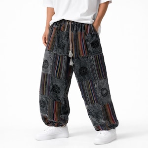 May include: Patchwork pants in shades of gray, featuring floral and striped patterns. The pants have a drawstring waist and a relaxed fit. The design incorporates various colors, including red, blue, and yellow. The pants are worn with white sneakers.