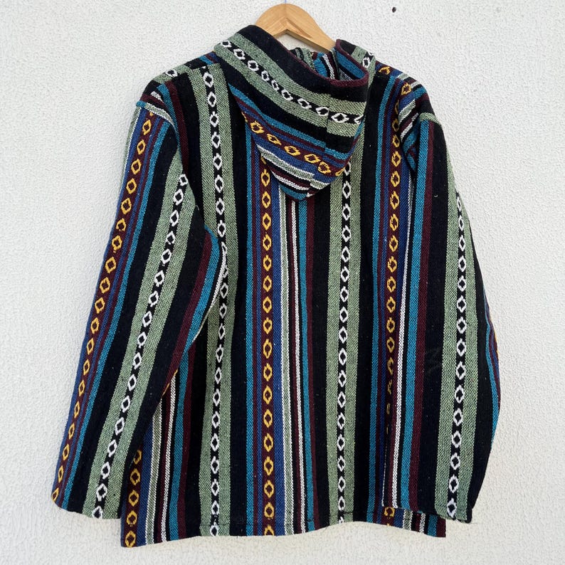 May include: A hooded jacket with a striped pattern in black, green, blue, and maroon. The jacket is hanging on a wooden hanger against a white wall. The stripes are vertical and feature geometric shapes.