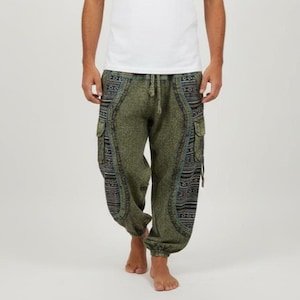 Op de afbeelding: Groene harembroek met patronen en twee cargozakken. De broek heeft een tailleband met trekkoord en is bij de enkels afgezet. De panelen hebben een blauw, zwart en wit geometrisch ontwerp.