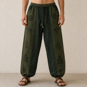 May include: Green and black patterned pants with a drawstring waist and pockets. The pants feature a vertical striped design with floral and Om symbol patterns. The pants are worn with brown sandals.