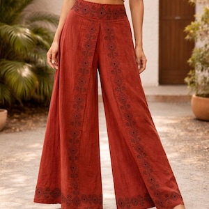 May include: Rust-colored wide-leg pants with intricate black embroidered patterns along the sides and waist. The pants are paired with a white crop top. The pants are made of a lightweight fabric, suitable for warm weather.