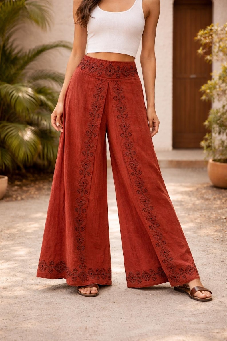 May include: Rust-colored wide-leg pants with intricate black embroidered patterns along the sides and waist. The pants are paired with a white crop top. The pants are made of a lightweight fabric, suitable for warm weather.