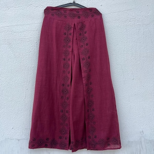 May include: Burgundy-colored wide-leg pants with a decorative geometric pattern in black. The pants are hanging on a black hanger. The fabric appears to be linen or a similar lightweight material.