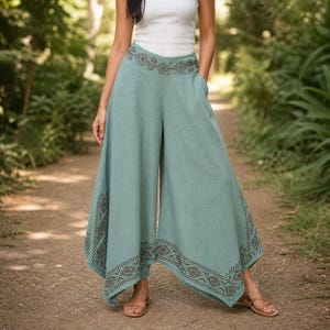 May include: Light teal palazzo pants with a wide leg design. The pants feature a decorative geometric pattern in a darker shade of teal along the pockets and hem. The pants are made of a lightweight fabric.
