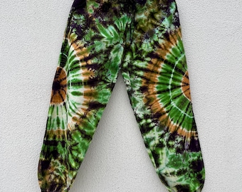 May include: Tie-dye pants in shades of green, brown, and white, hanging on a wooden hanger. The pants feature a drawstring waist and a unique spiral pattern. The fabric appears to be lightweight and suitable for casual wear.