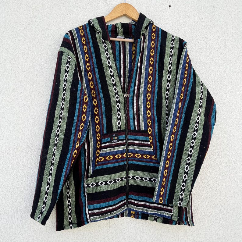 May include: A hooded zip-up jacket with a colorful striped pattern. The jacket features vertical stripes in black, green, blue, and red, with a front pocket and a wooden hanger. The text "THE GOOD VIBES" is visible on the pocket.
