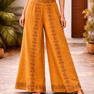 May include: Mustard-colored wide-leg pants with intricate geometric patterns down the sides. The pants have a high waist and are paired with a white crop top. The pants are made of a lightweight fabric, perfect for warm weather.