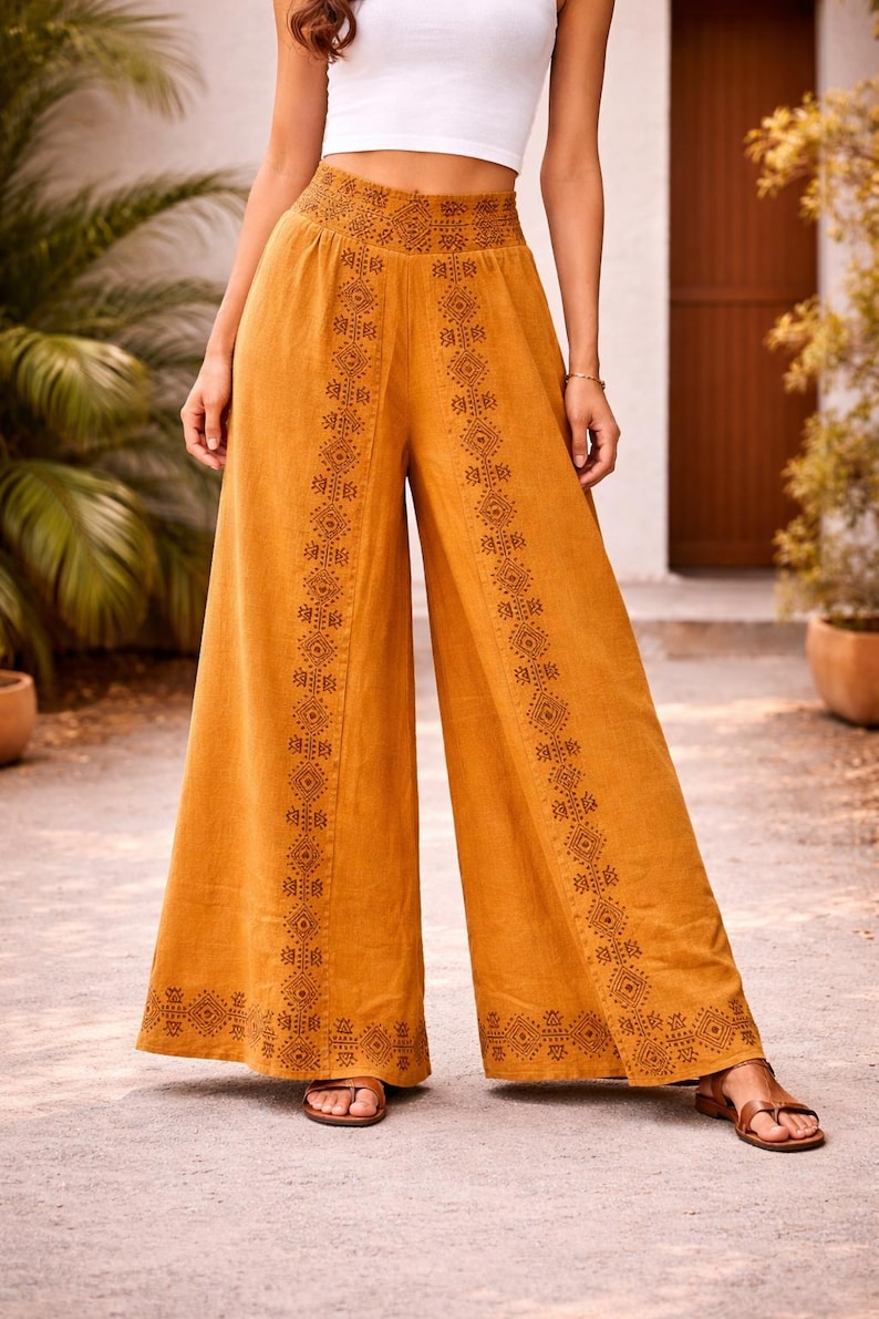 May include: Mustard-colored wide-leg pants with intricate geometric patterns down the sides. The pants have a high waist and are paired with a white crop top. The pants are made of a lightweight fabric, perfect for warm weather.