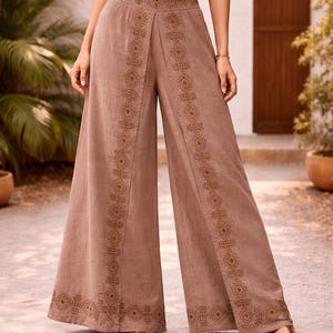 May include: Wide-leg, brown pants with intricate embroidered patterns down the front and along the sides. The pants have a high waist and are paired with a white crop top. The model is wearing brown sandals.