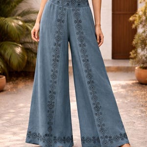 May include: Wide-leg, blue pants with intricate black geometric patterns along the sides and waistband. The pants are made of a soft fabric and are worn with sandals. The pants are a stylish addition to any wardrobe.