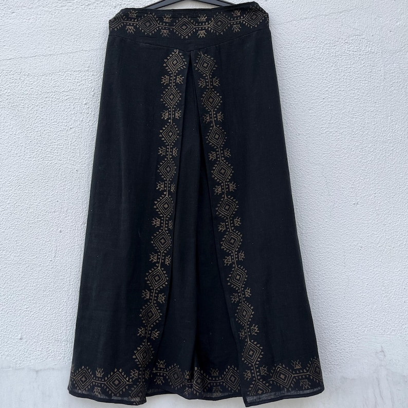 May include: Black skirt with a split front and intricate geometric embroidery in a gold color. The skirt has a high waist and a flowing, A-line silhouette. The embroidery is concentrated along the edges and the split, adding a decorative element to the garment.