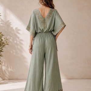 May include: Sage green jumpsuit with a V-neckline and wide-leg pants. The top features embroidered detailing along the neckline and sleeves. The waist is elasticized. The bottom of the pants also has embroidered detailing.