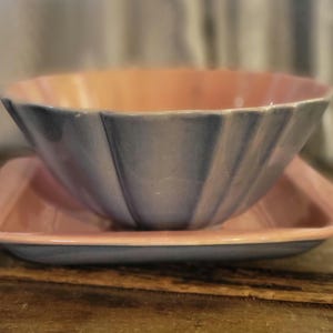 May include: A two-toned ceramic bowl and tray set. The bowl is a light blue with a scalloped edge and a peach interior. The tray is a matching peach color with a blue rim. The set is likely vintage or retro.