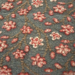 Könnte beinhalten: Nahaufnahme eines Textils mit einem sich wiederholenden Blumenmuster. Die Blumen sind rot und weiß, vor einem grauen Hintergrund. Braune, strukturierte Linien bilden ein Gitter.