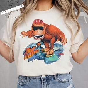 a woman wearing a t - shirt with a picture of a monkey riding a surf