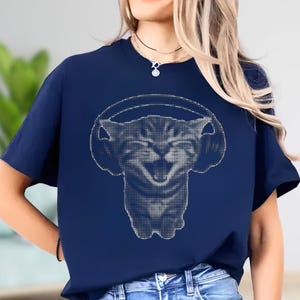 May include: Navy blue t-shirt featuring a white graphic of a cat wearing headphones. The cat's face is smiling, and the design is made up of small dots. The shirt has short sleeves and a crew neck.