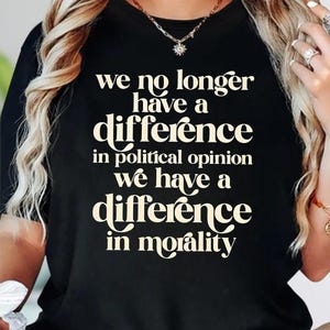 May include: A black t-shirt featuring cream-colored text that reads: we no longer have a difference in political opinion we have a difference in morality. The shirt has a crew neckline and short sleeves, displaying the printed message on the front.