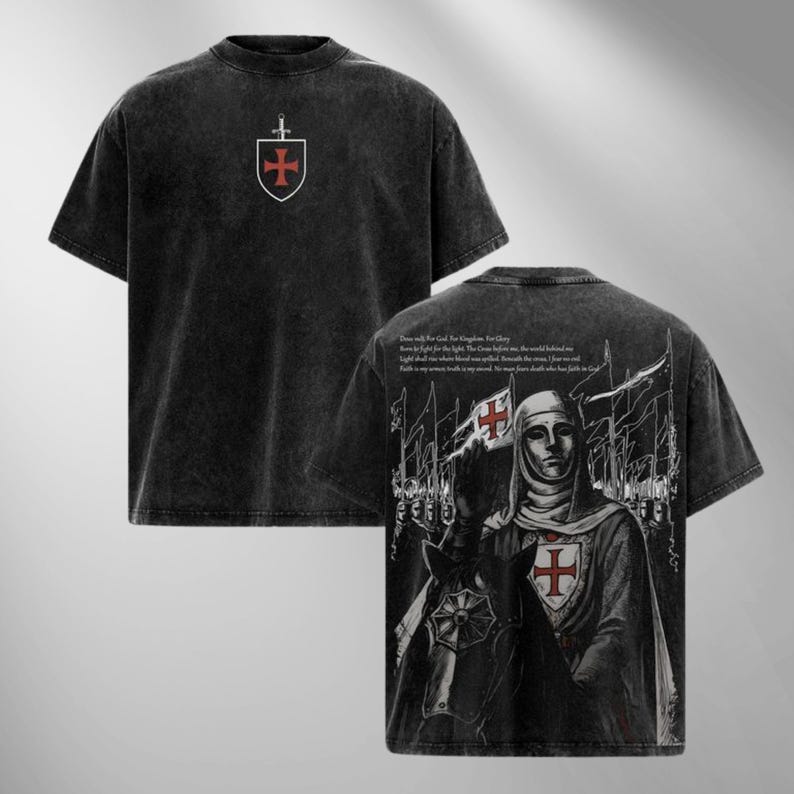 May include: Dark gray t-shirt with a distressed look. The front features a shield and sword emblem with a red cross. The back displays a detailed illustration of a knight holding a flag with a red cross, along with text.